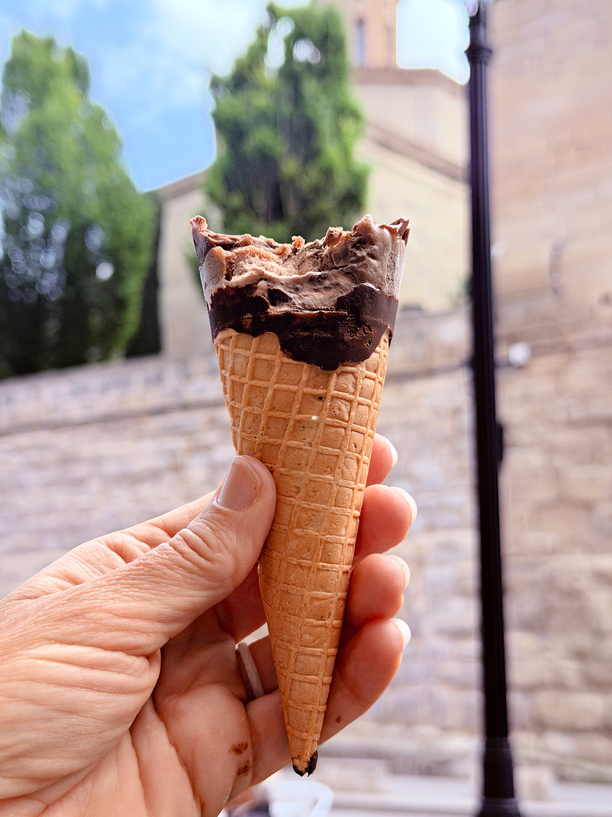 Hand holding a chocolate ice cream cone along a stone street in Spain.