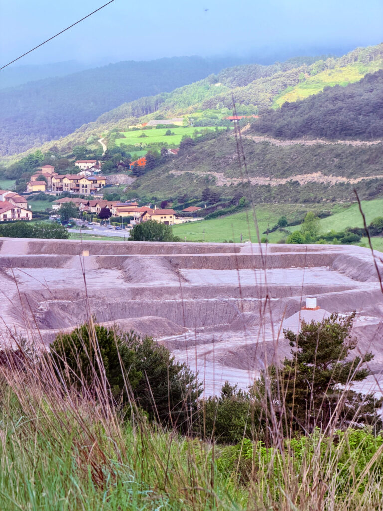 Large open-pit magnesium quarry below a green mountain village in Navarra, Spain.