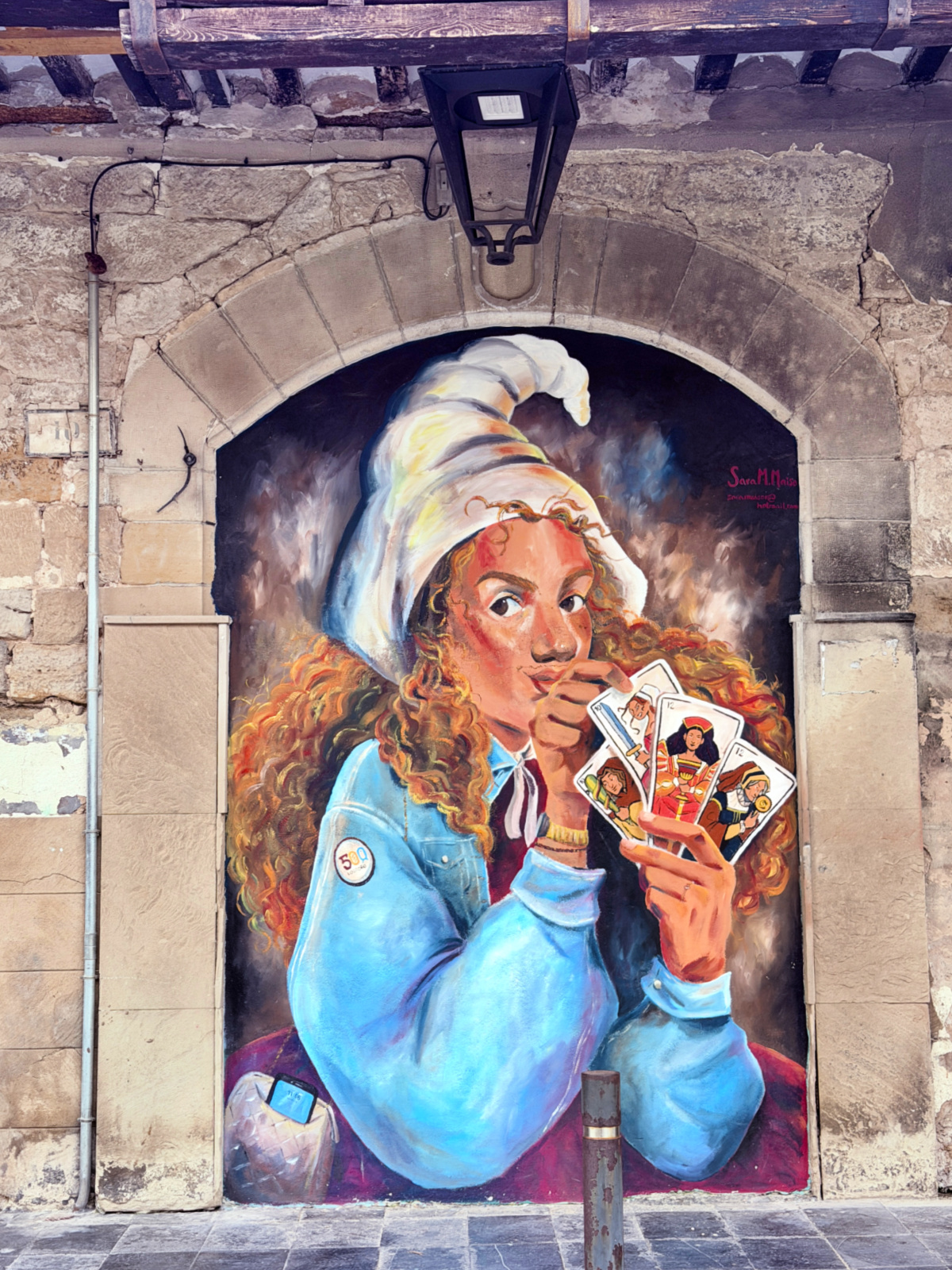 Colorful mural of a woman holding cards painted inside a stone archway.