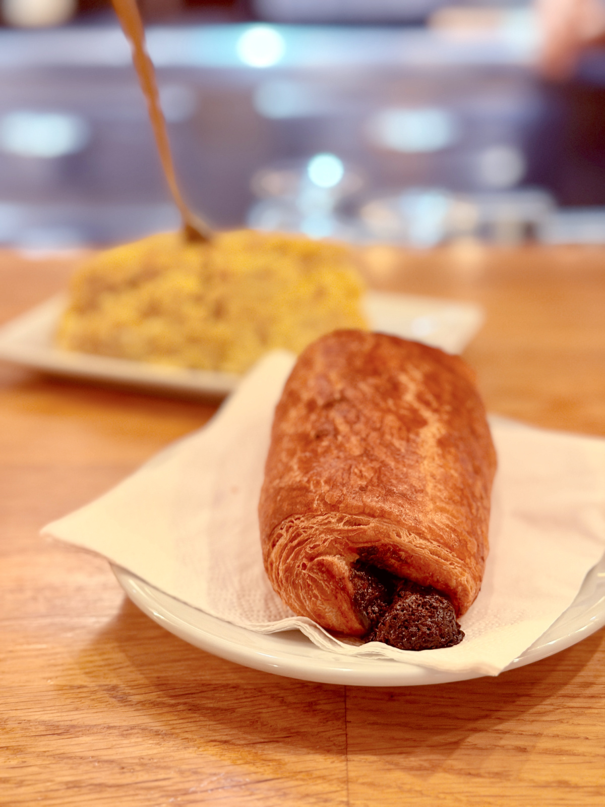 Pain au chocolat served on a white plate with coffee being poured in the background.