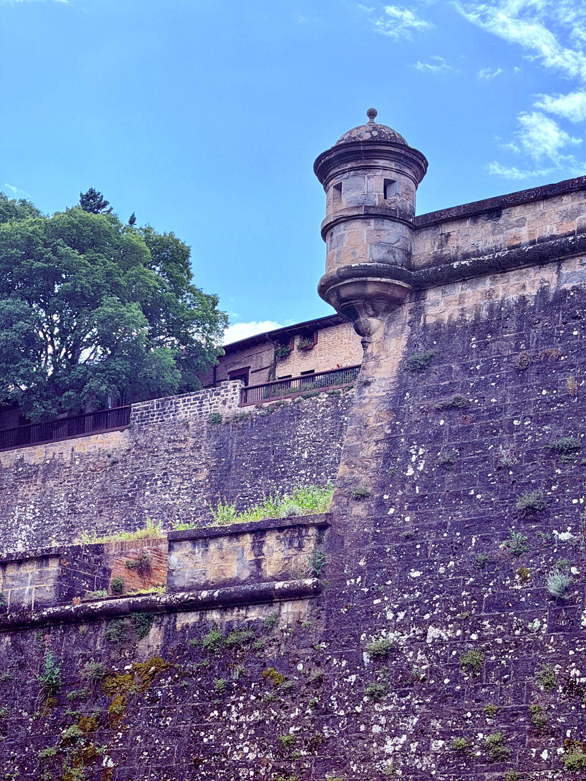 Historic stone fortification wall and rounded guard tower beneath a blue sky in Pamplona.