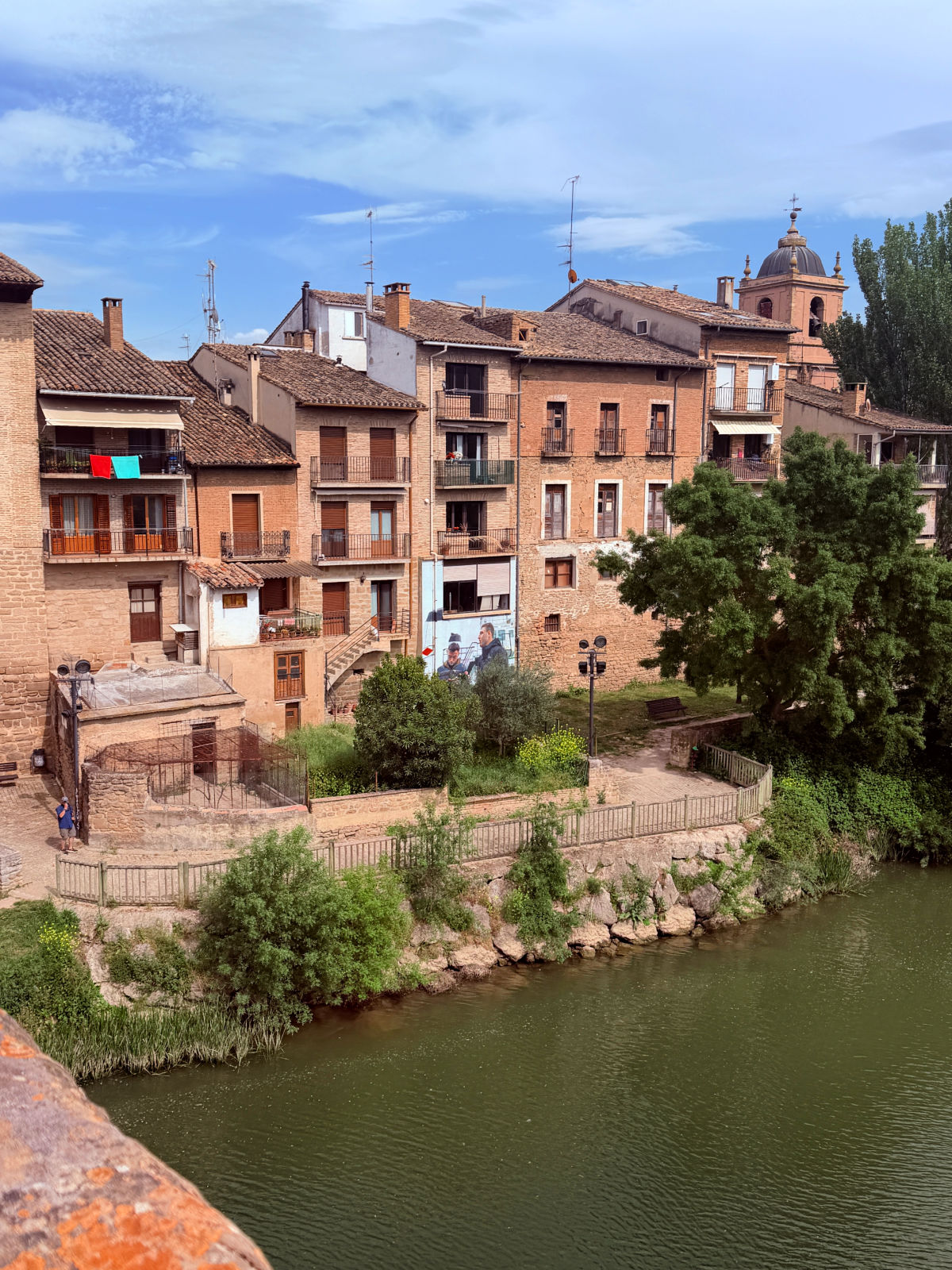 Historic buildings and a church tower beside the Arga River in Puente la Reina.