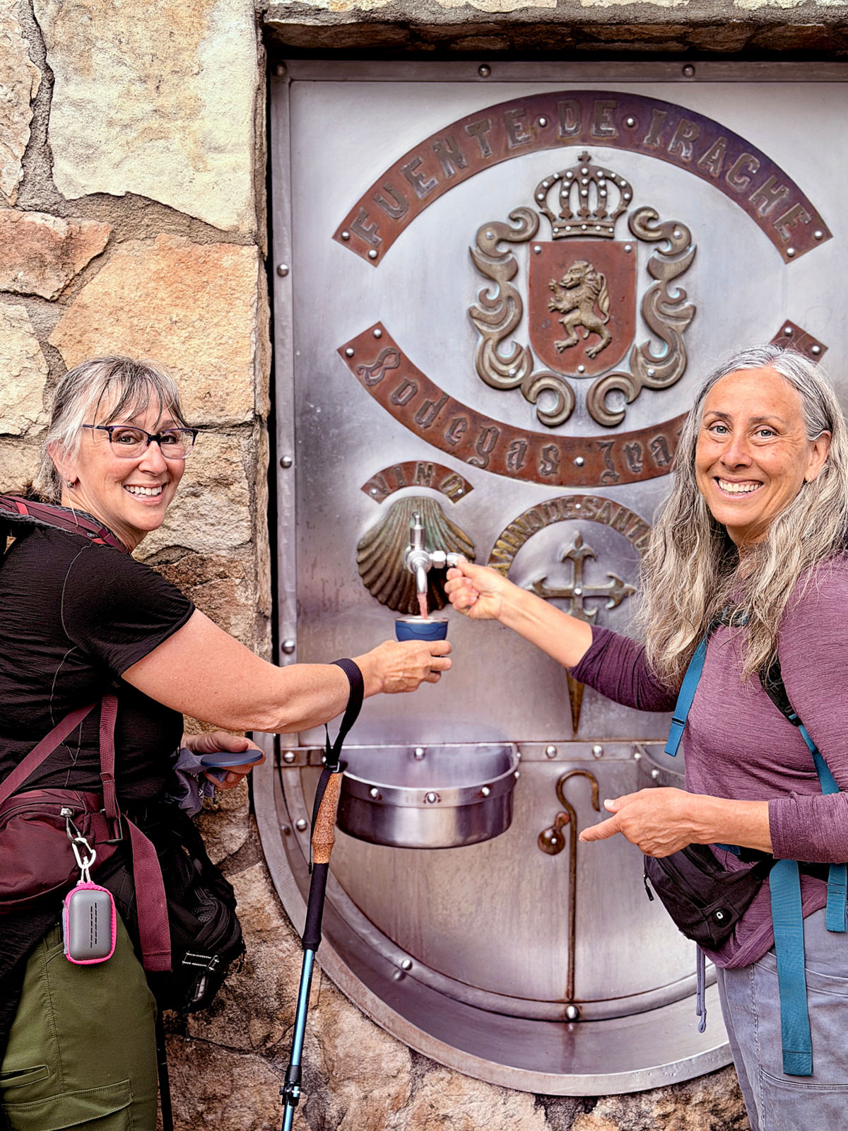 Two smiling pilgrims filling cups at the wine fountain outside Bodegas Irache.