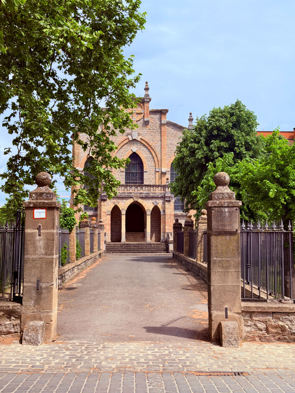 Tree-lined entrance leading to a historic Gothic-style stone building in Pamplona.