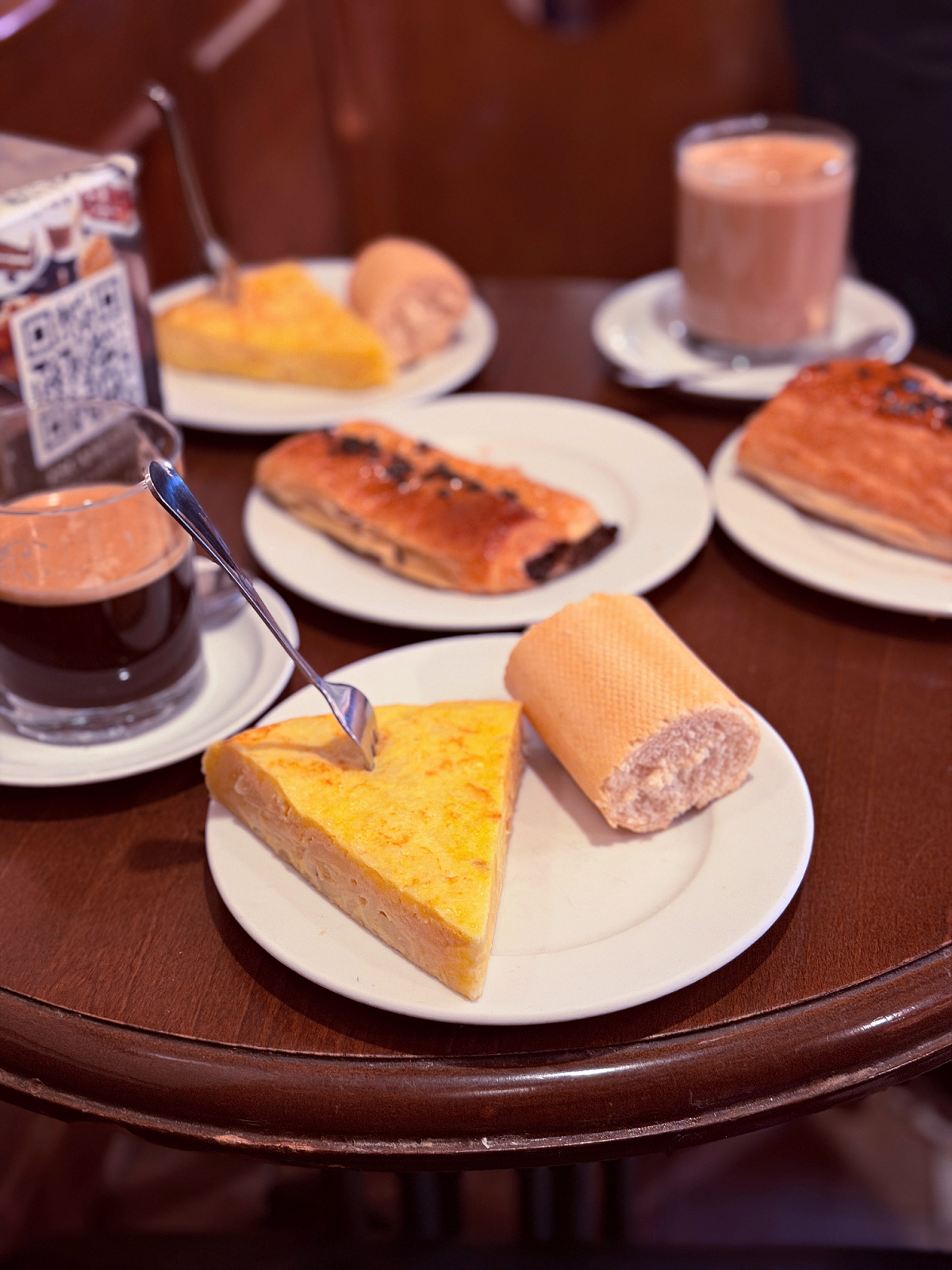 Slice of Spanish tortilla served with toast and hot drinks at a café.