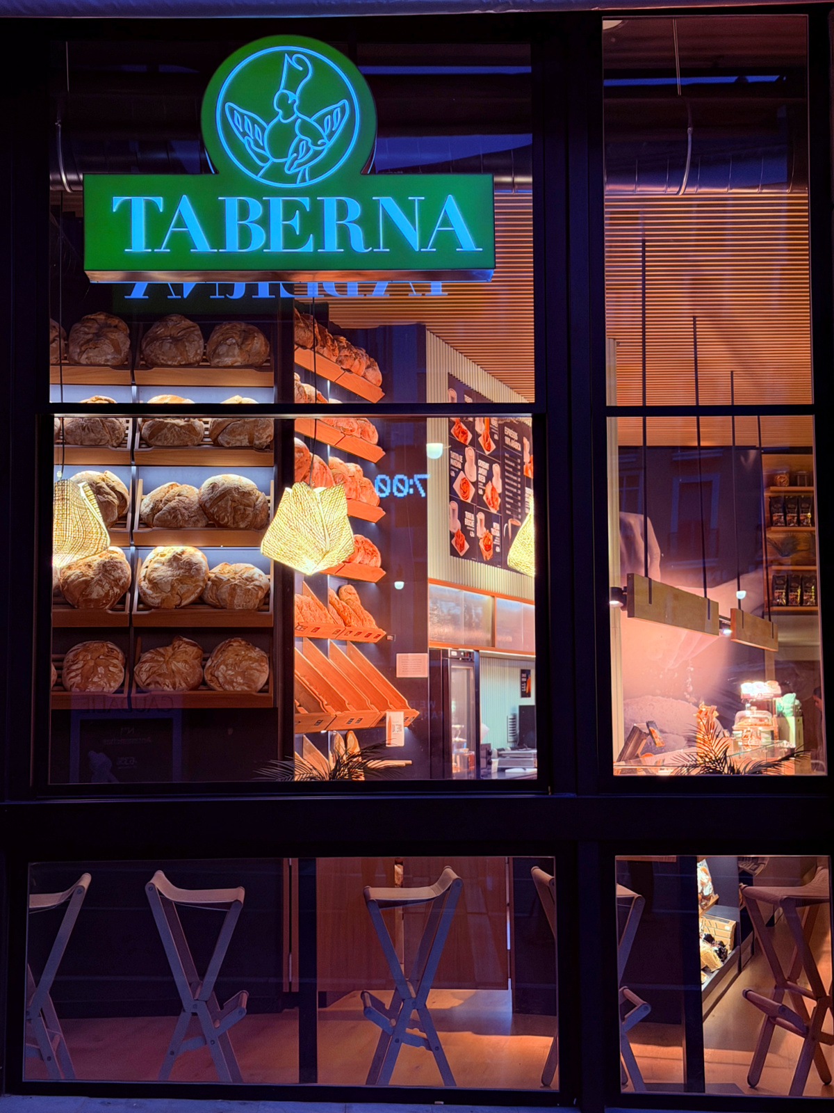 Illuminated Taberna storefront with loaves of bread displayed inside.