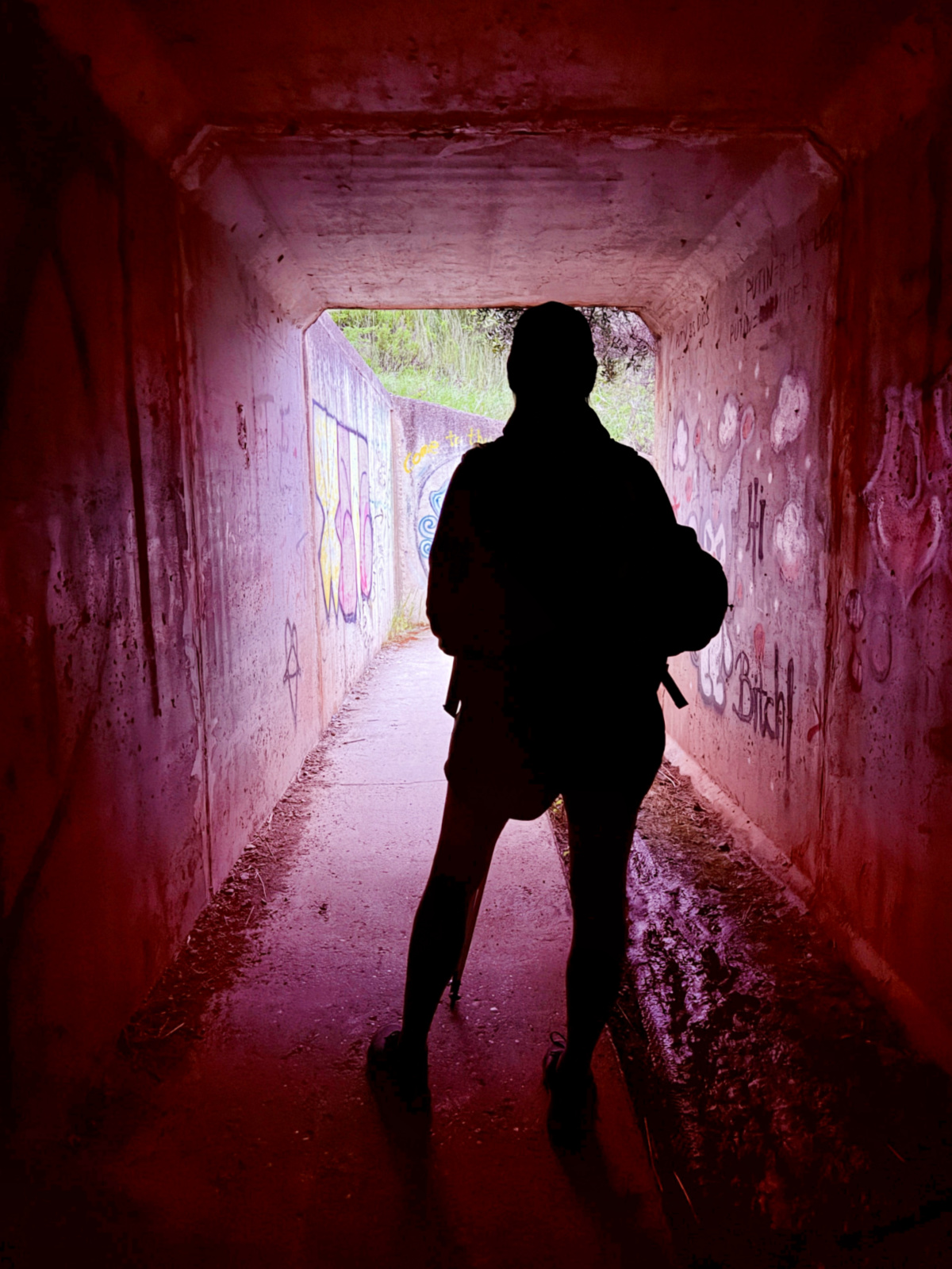 Silhouette of a Camino pilgrim walking through a red-walled pedestrian tunnel.