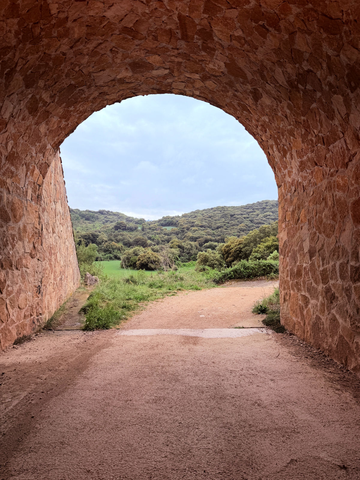 Camino trail passing through a rounded stone tunnel into the countryside.