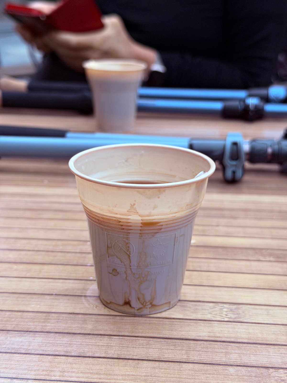 Small plastic cup of coffee from a vending machine resting on an outdoor table.