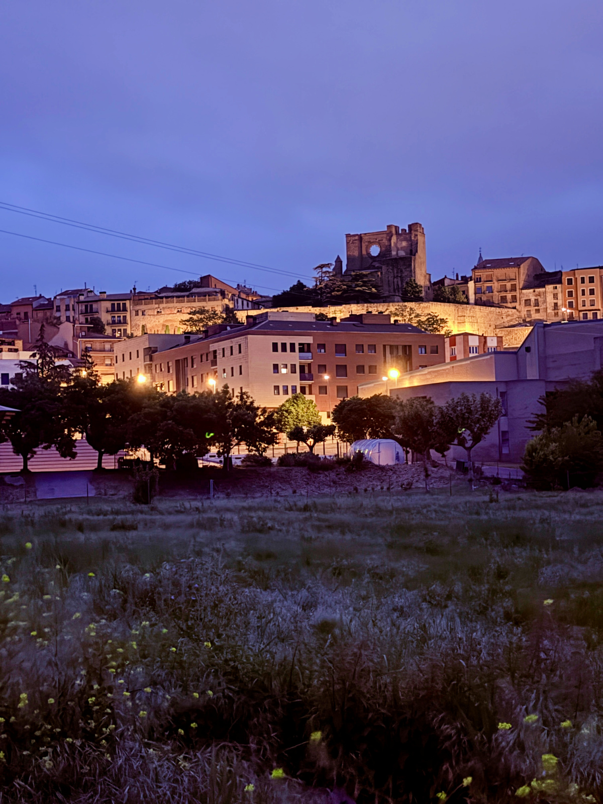 Illuminated buildings of Viana on a hillside beneath the blue early-morning sky.