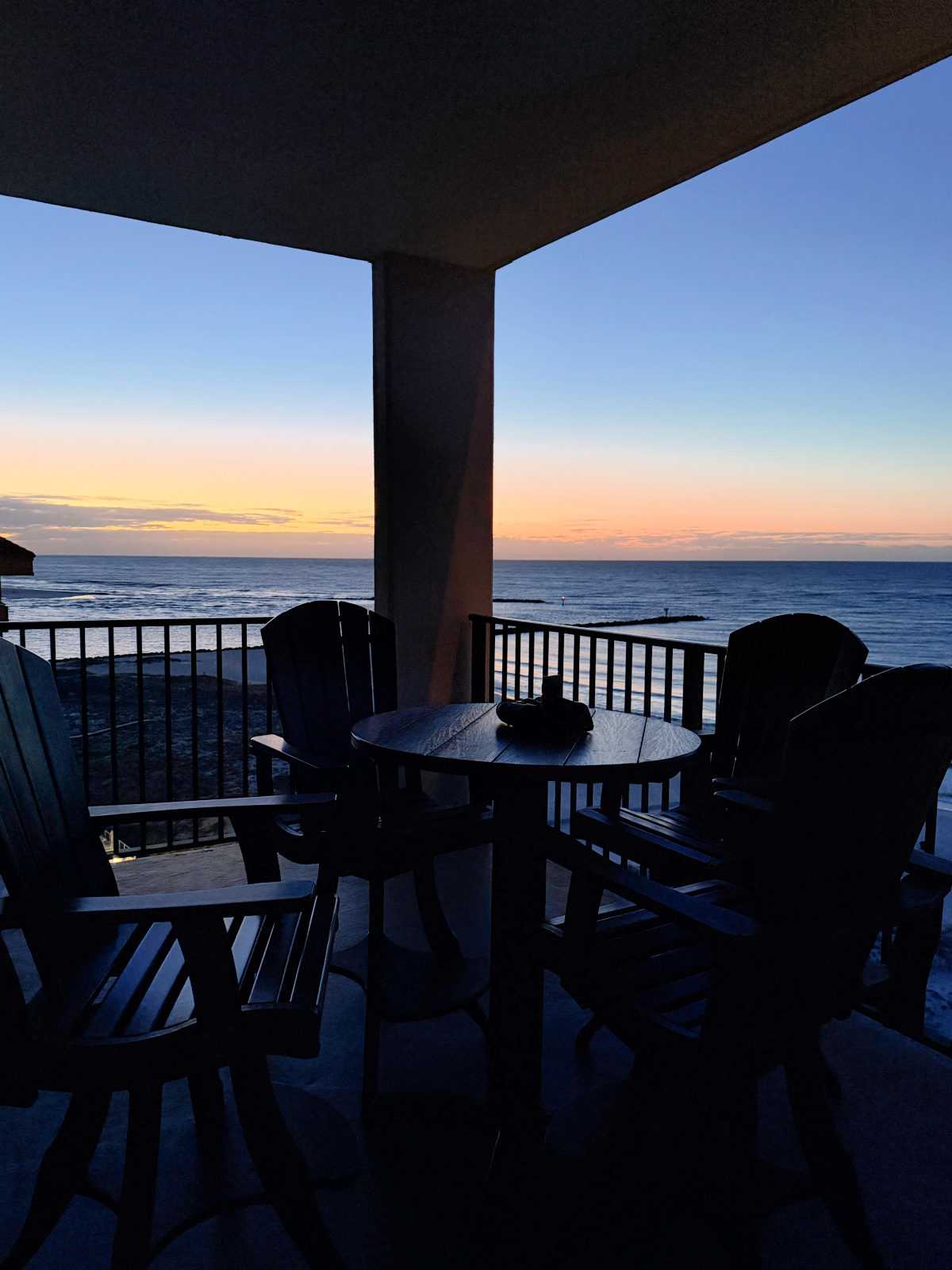 Silhouetted balcony table and four chairs overlooking the Gulf of Mexico at sunrise from a Phoenix East II condo in Orange Beach, Alabama.