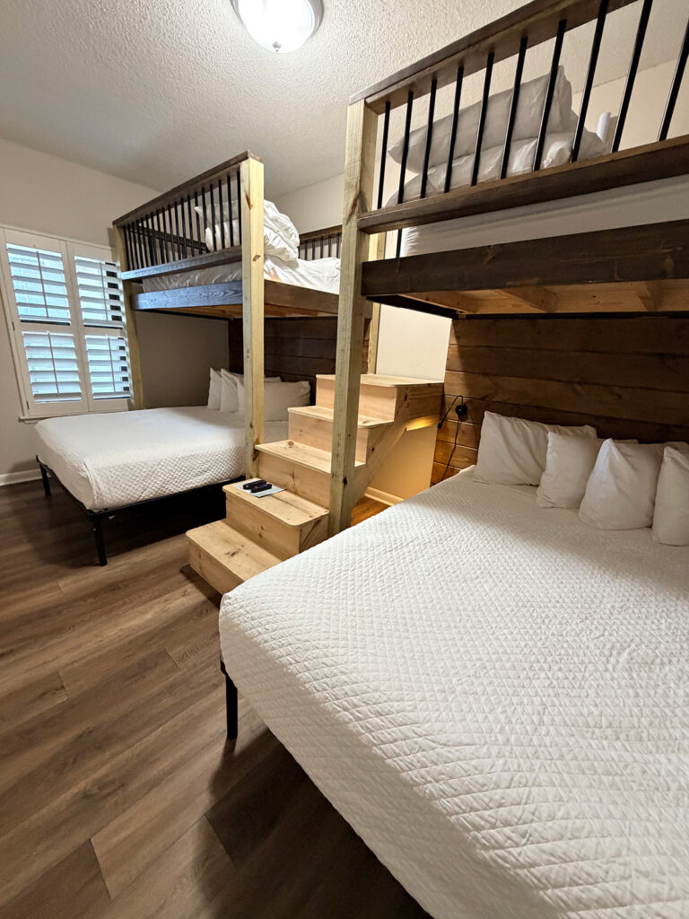 Bunk room with two queen beds, loft beds above, and wooden stairs in a three-bedroom Orange Beach condo.