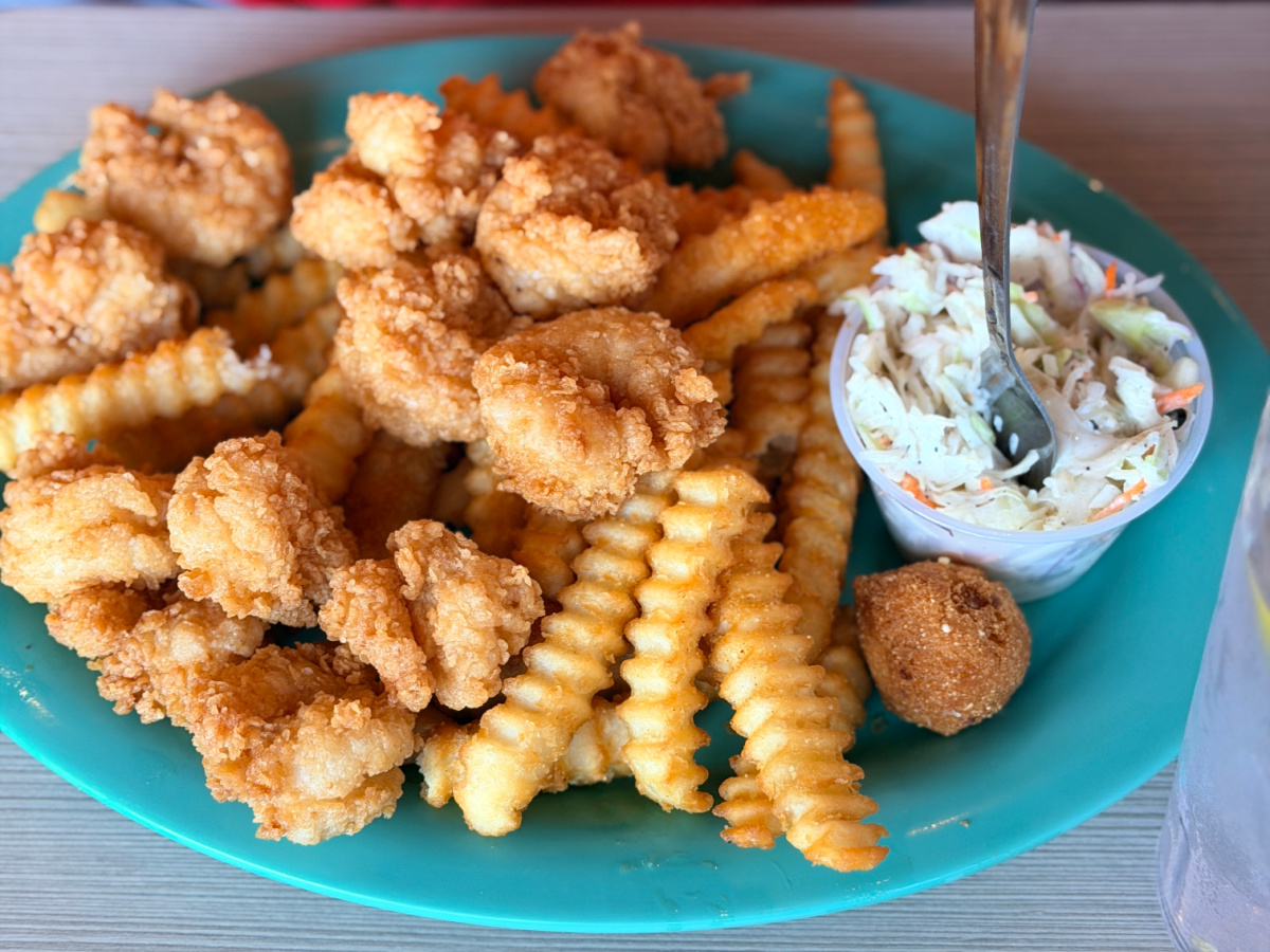 Fried shrimp platter with crinkle-cut fries, coleslaw, and a hush puppy on a teal plate.