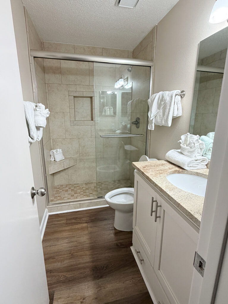 Condo bathroom with a tiled walk-in shower, glass sliding door, and white vanity.