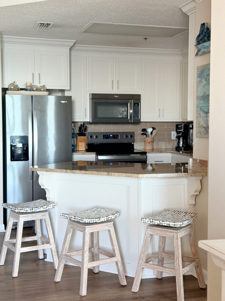 Condo kitchen with white cabinets, stainless steel appliances, a granite counter, and three barstools.