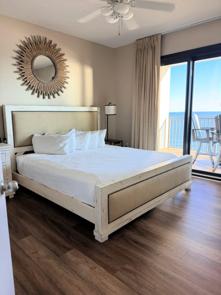 King bed with a sunburst mirror above it and a sliding door to a balcony overlooking the Gulf.