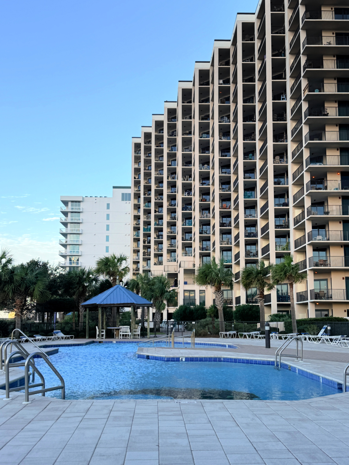 Outdoor pool with a gazebo in front of a tall Phoenix condo tower in Orange Beach.