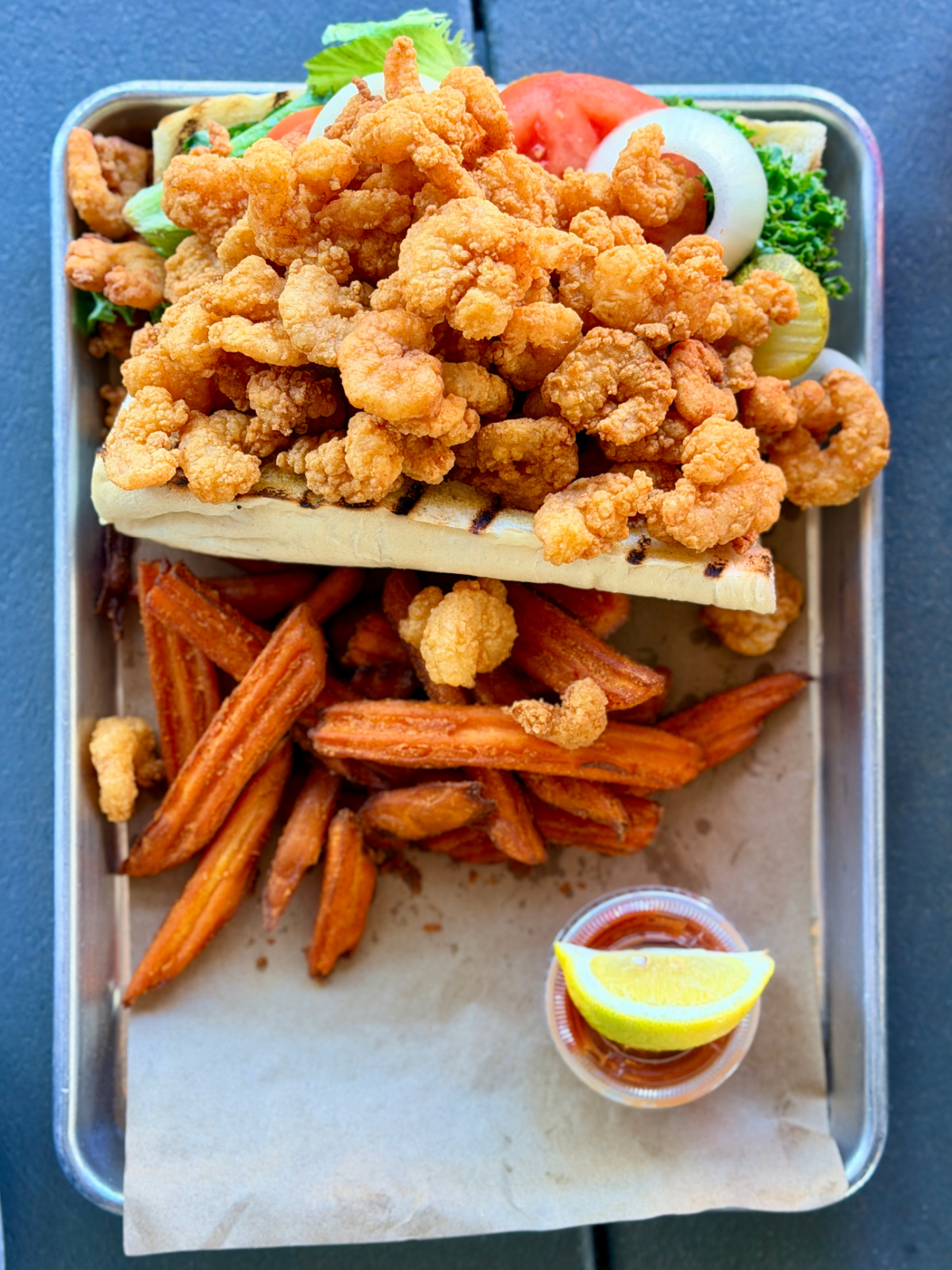 Fried shrimp Po' Boy piled high with shrimp, served with sweet potato fries and cocktail sauce.